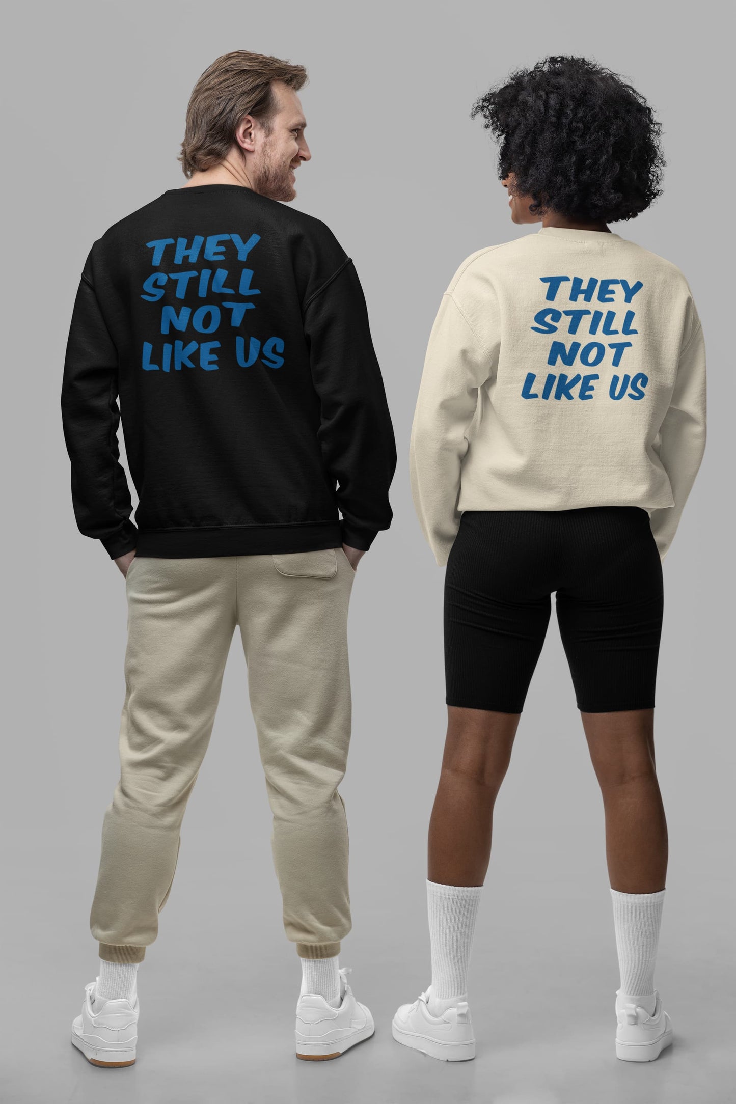 Couple wearing black and sand they still not like us sweatshirts showing back print design