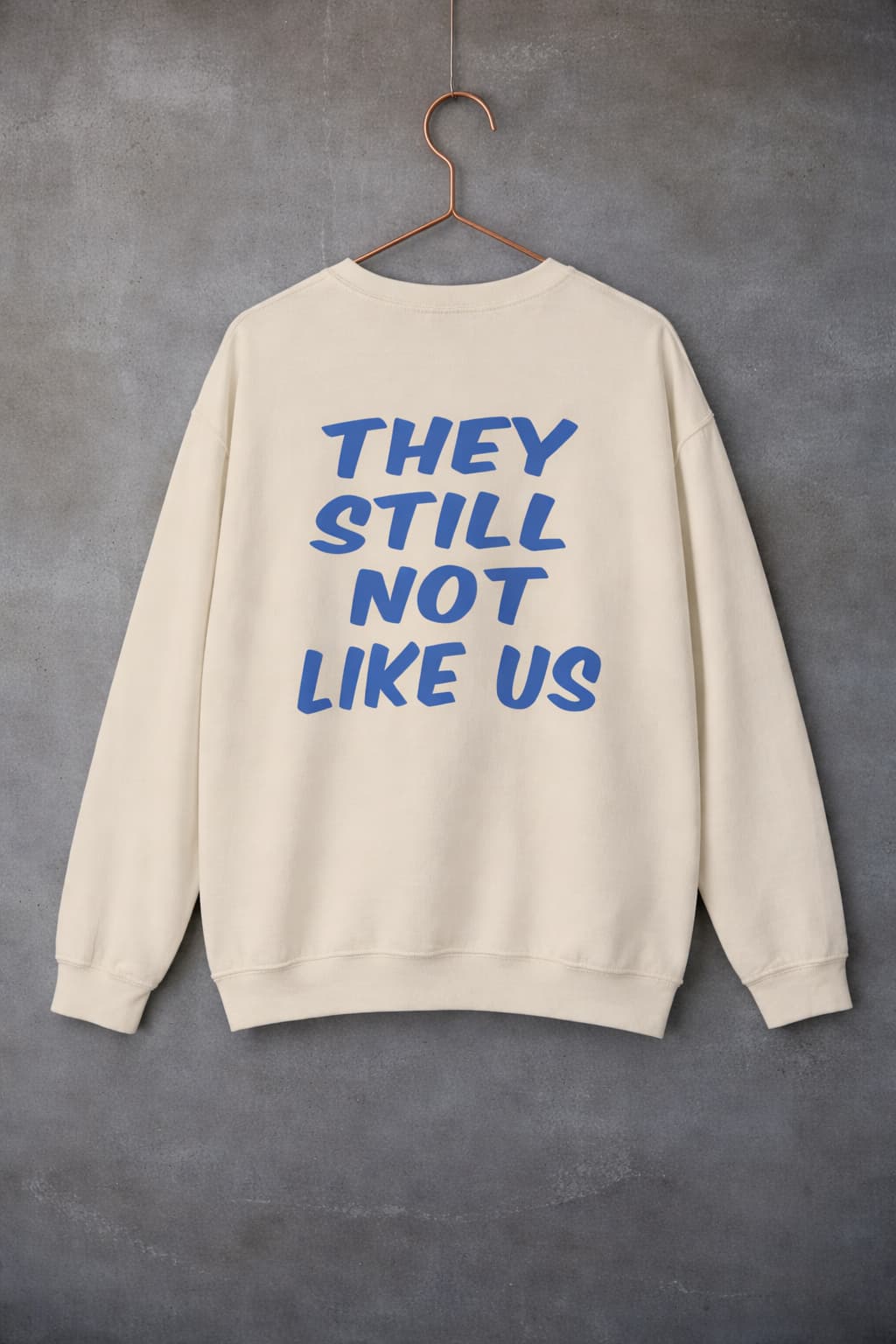 Black they still not like us crewneck sweatshirt hanging on hanger against concrete wall